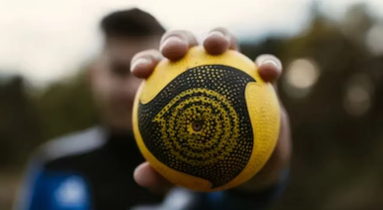 photo of male holding a yellow juggling ball to the camera